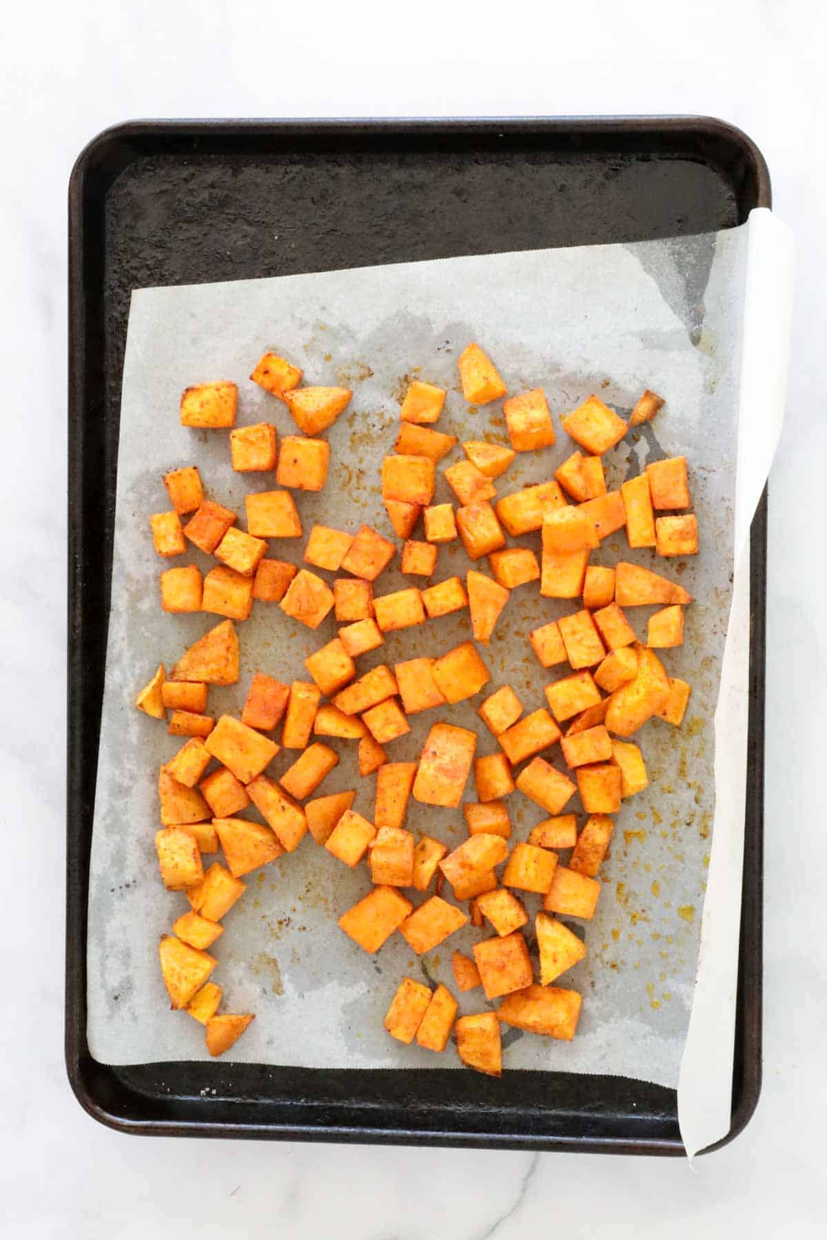 The baked sweet potato cubes on the lined baking sheet.