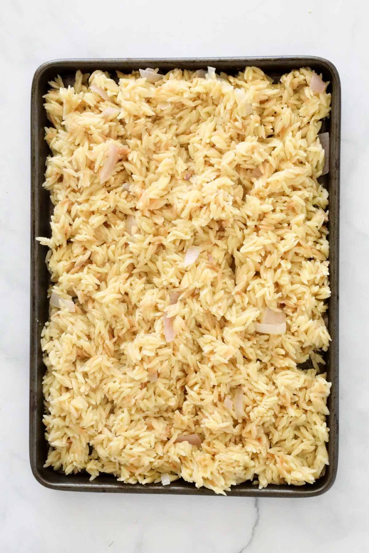 The grains of cooked pasta spread out on a tray to cool.