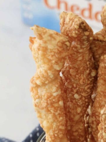 Crunchy baked cheese twists in a jar in front of a packet of cheddar cheese.