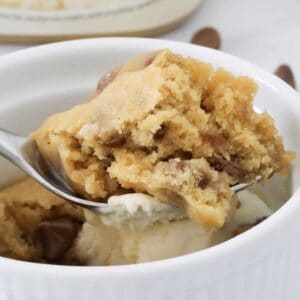 A spoon holding a microwave cookie cooked in a mug.