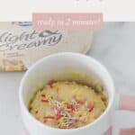 A vanilla mug cake with sprinkles on top, in front of a tub of ice cream.