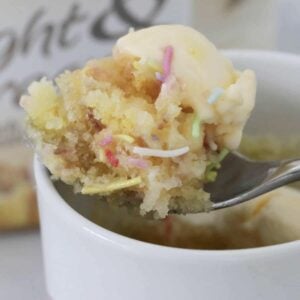 A spoon holding a fluffy vanilla cake with sprinkles and ice cream.