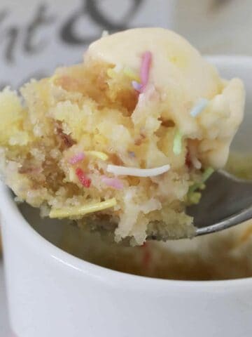 A spoon holding a fluffy vanilla cake with sprinkles and ice cream.
