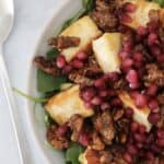 A bowl filled with a grilled halloumi salad with spinach, candied walnuts and pomegranates.