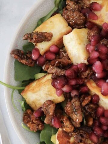 A bowl filled with a grilled halloumi salad with spinach, candied walnuts and pomegranates.