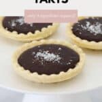 Mini chocolate tarts, sprinkled with sea salt, served on a white cake stand.