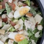 A bowl filled with chicken caesar salad with bacon, parmesan, egg and croutons.