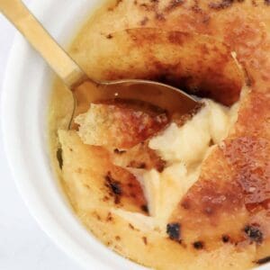 An overhead shot of a spoon cracking the sugar top on a creme brulee dessert.