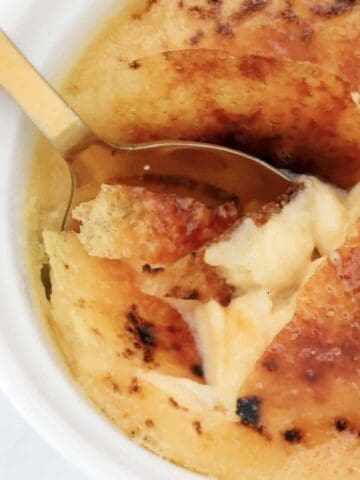 An overhead shot of a spoon cracking the sugar top on a creme brulee dessert.