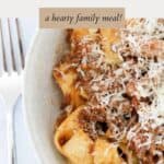 A portion of lamb ragu with parpadelle noodles, and a sprinkle of parmesan in a white bowl.