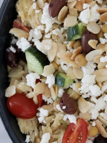 An overhead shot of a bowl of risono salad with Greek flavours including lemon, feta and tomato.