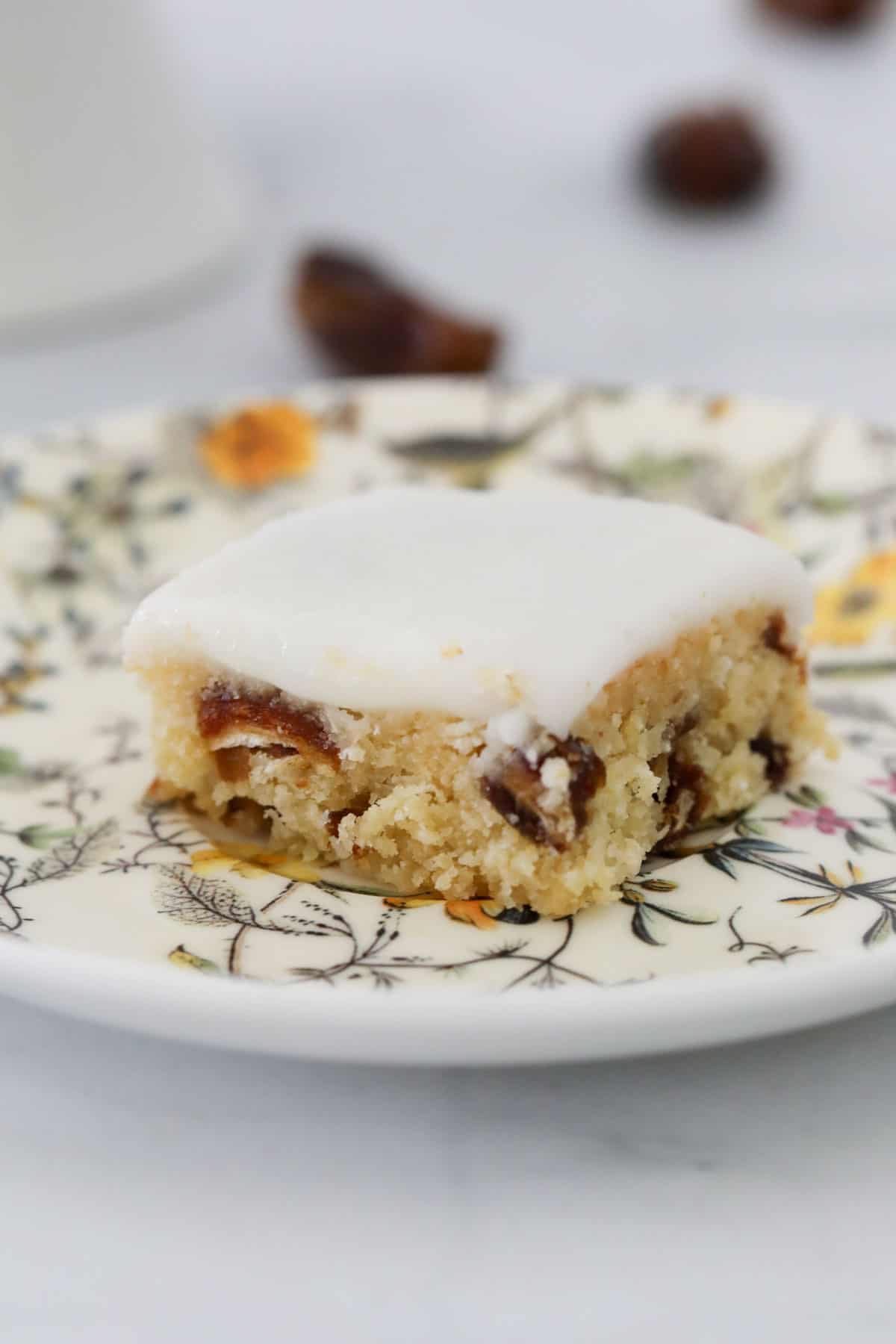 A piece of date slice with lemon icing, on a pretty floral plate.