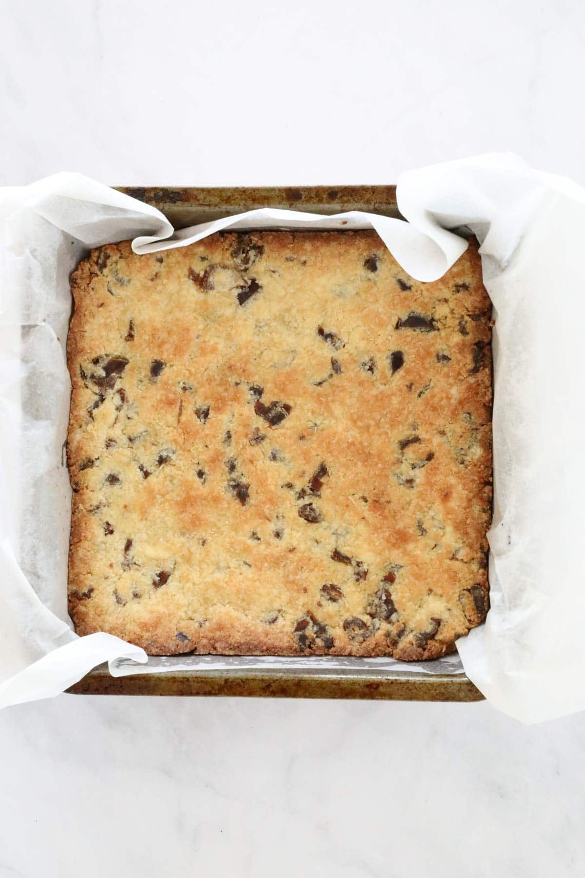 Overhead shot of baked date slice in a square lined baking tin.