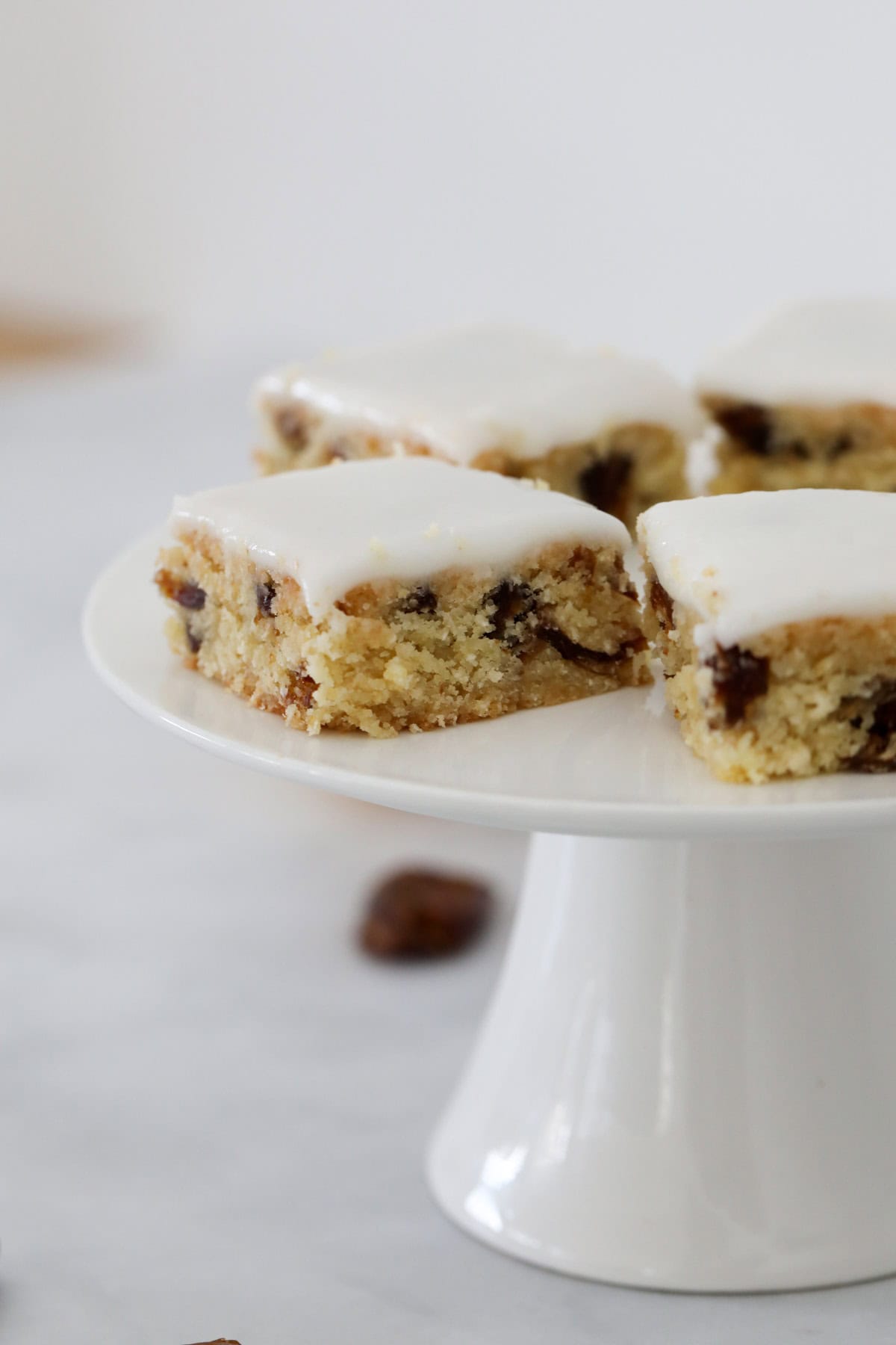 Squares of a chewy date slice on a white cake stand.