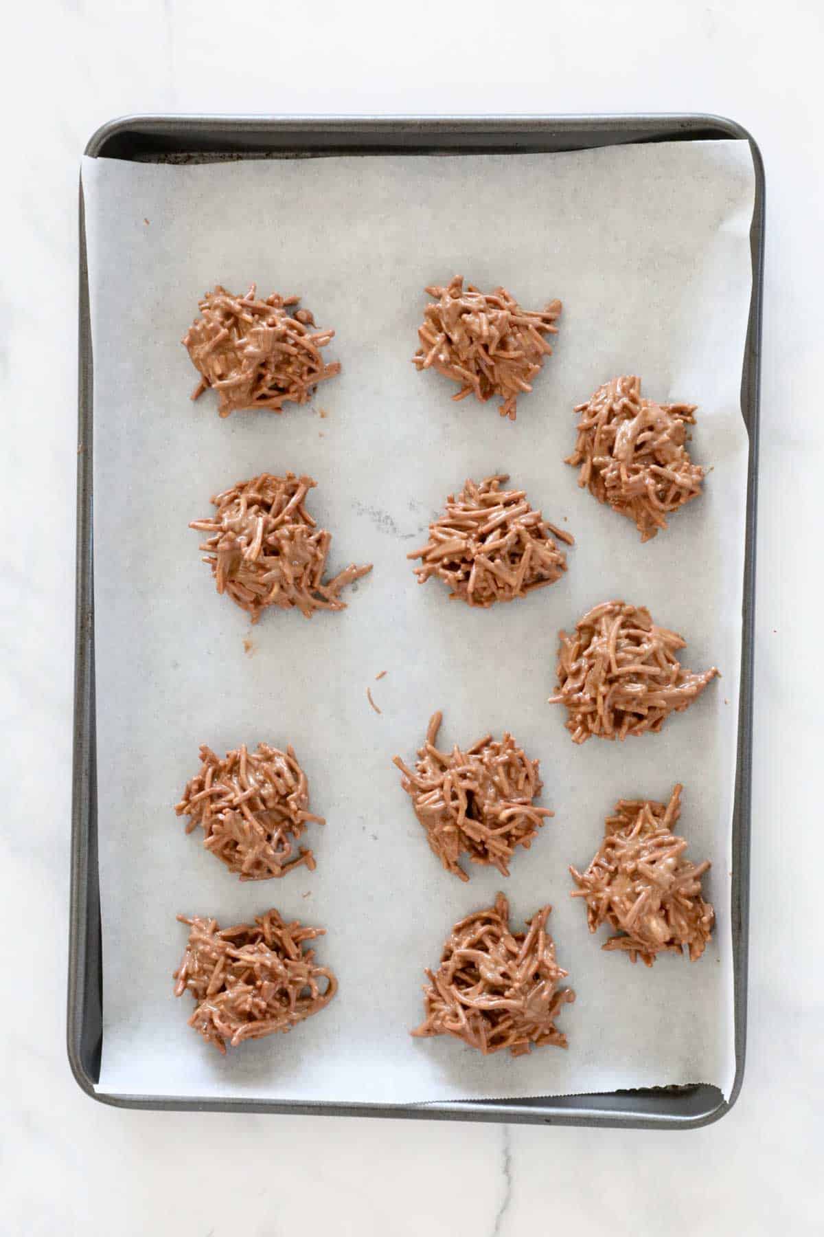 Spoonfuls of chocolate and noodle mix placed on baking paper on a tray.