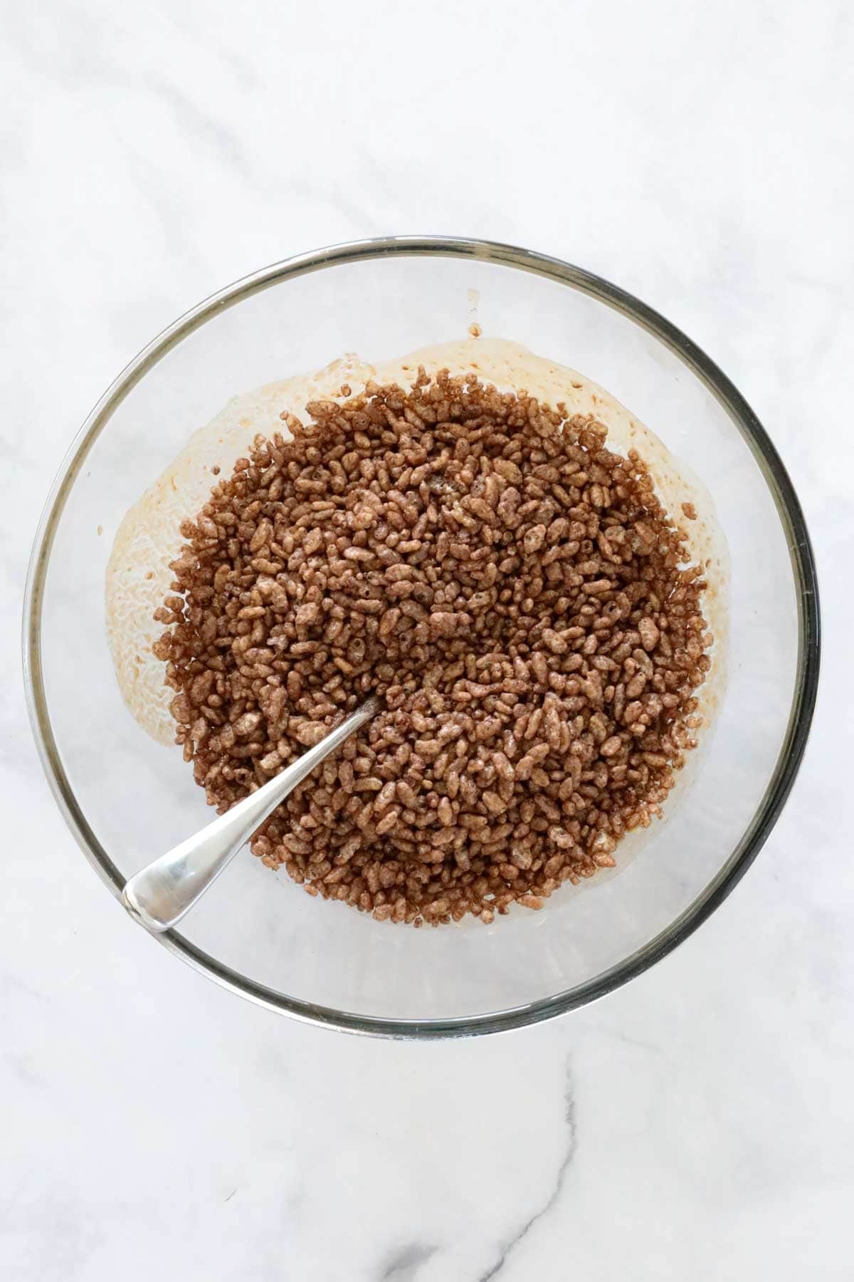 Coco Pops added to melted butter mixture in a large glass bowl.