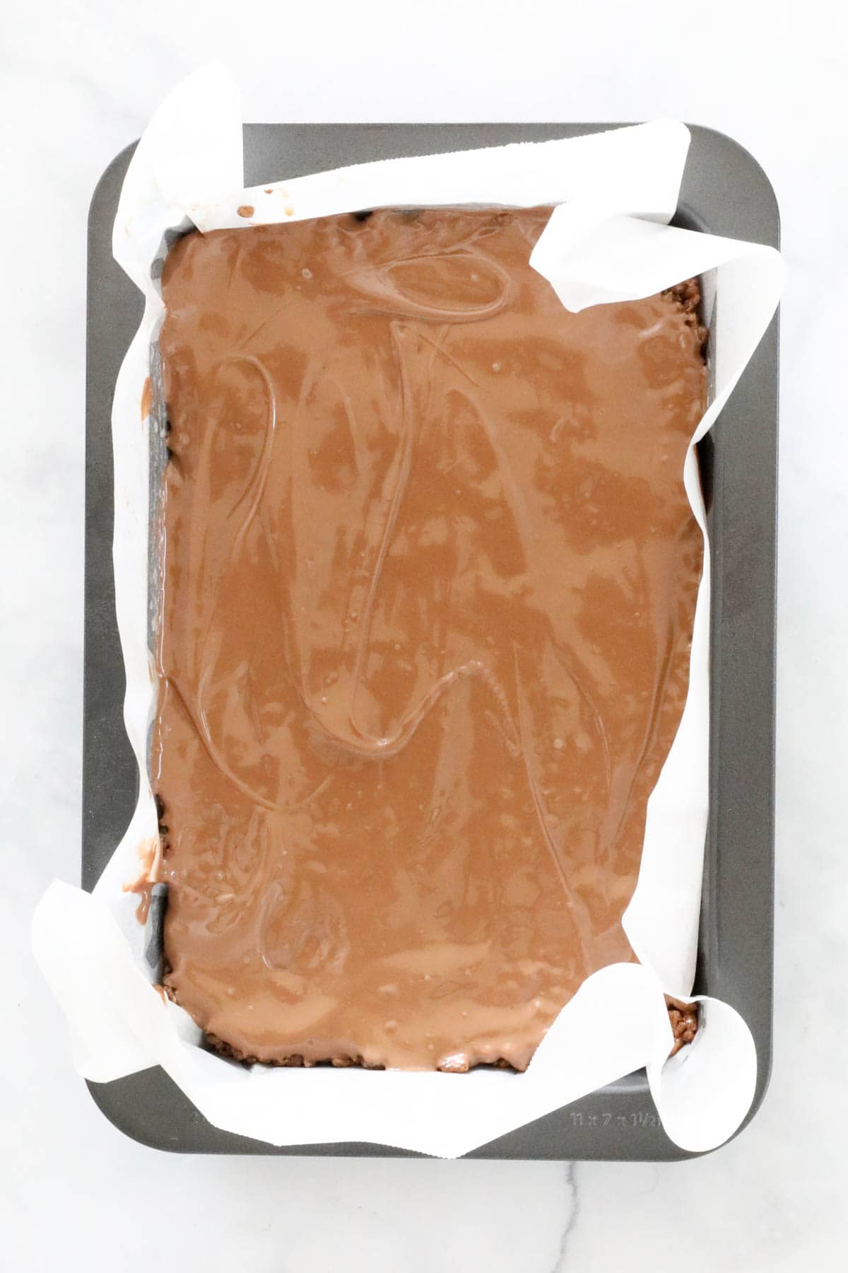 Melted milk chocolate spread over the slice in the lined slice tin.