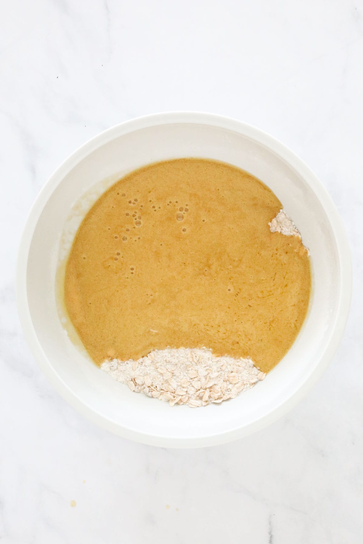 Butter and golden syrup mixture poured over dry ingredients in a mixing bowl.