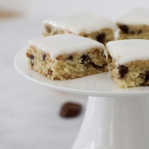 Squares of a chewy date slice on a white cake stand.