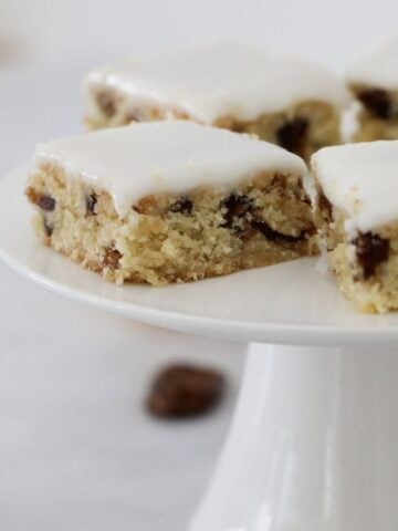 Squares of a chewy date slice on a white cake stand.