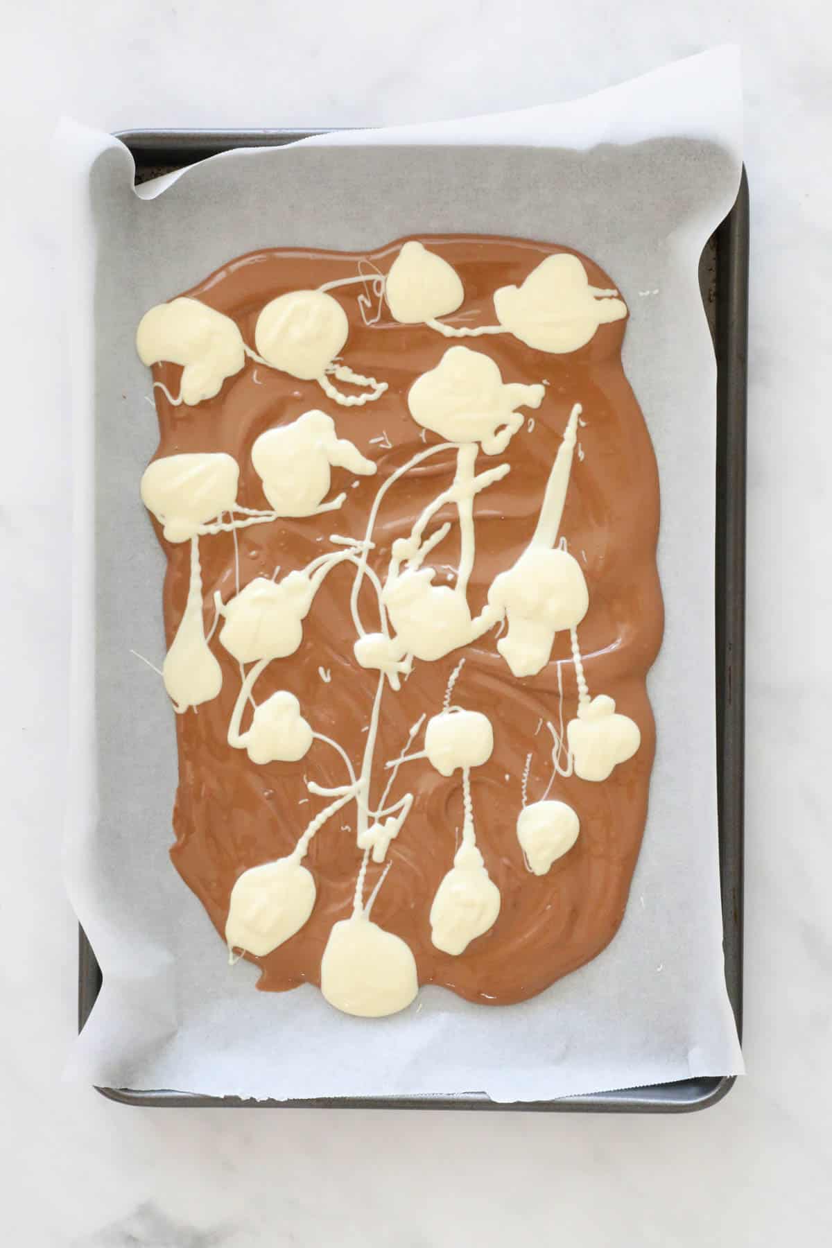 Dollops of melted white chocolate spooned on to melted milk chocolate spread on baking paper.