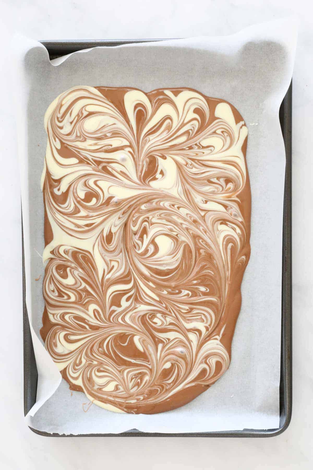 Milk chocolate melted and spread out on baking paper, with dollops of melted white chocolate swirled through.