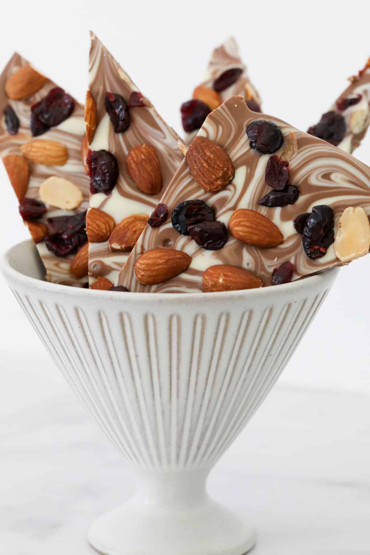 A white conical bowl with shards of chocolate, fruit and nut bark in it.