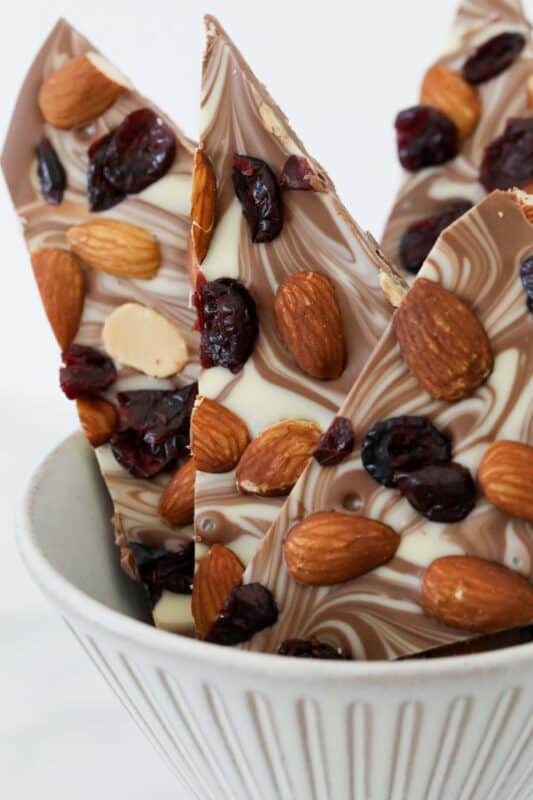 Shards of chocolate bark covered in almonds and cranberries, placed in a bowl.