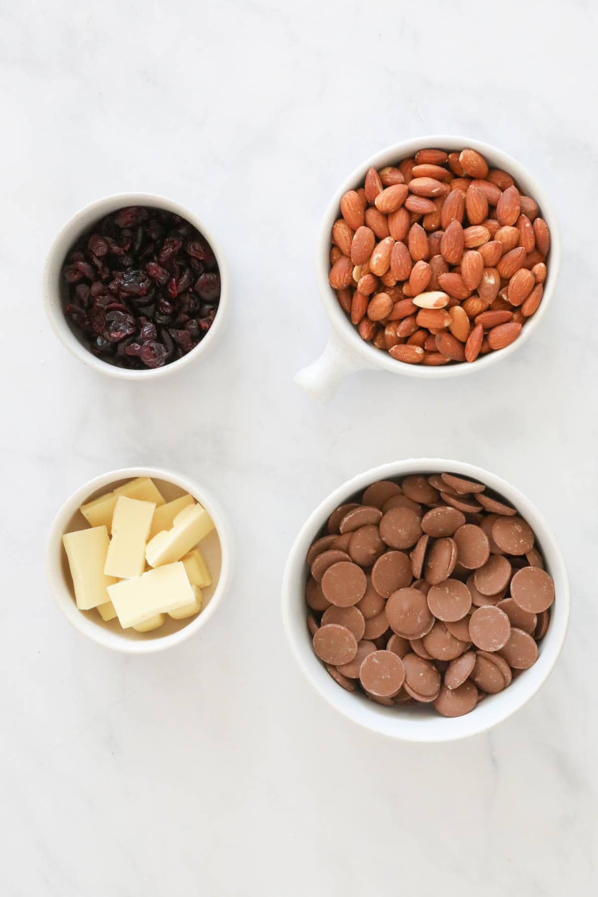 Chocolate, almonds and cranberries placed on a white bench.