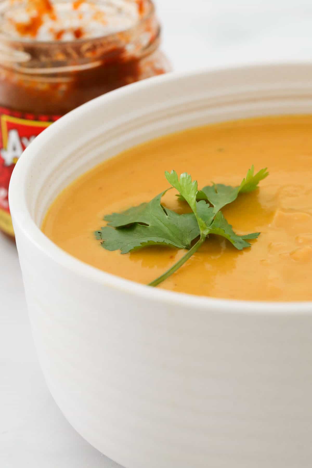 A piece of coriander on top of a bowl of Thai Pumpkin Soup.