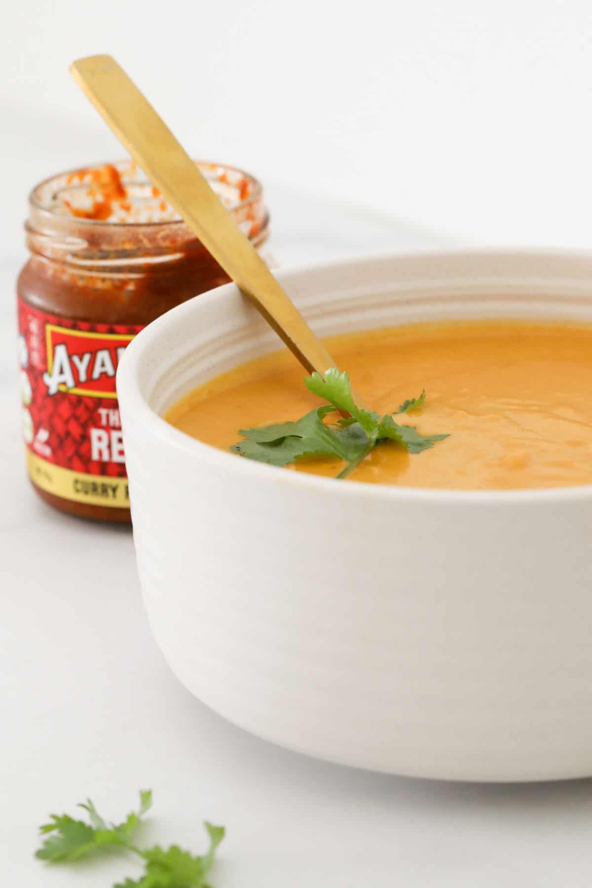 A white bowl of soup with a jar of red curry paste in the background.