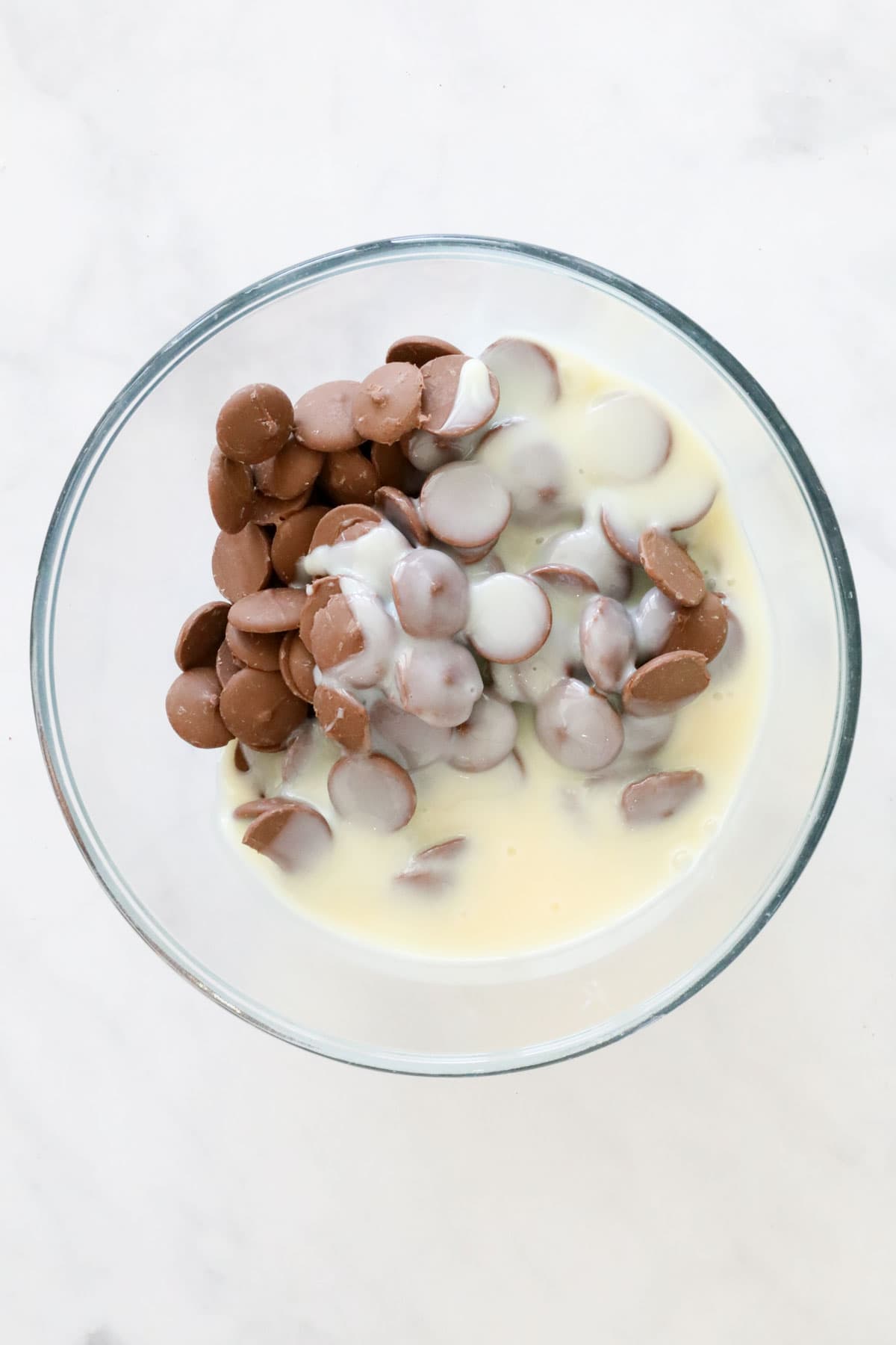 Chocolate melts and sweetened condensed milk in a glass bowl.