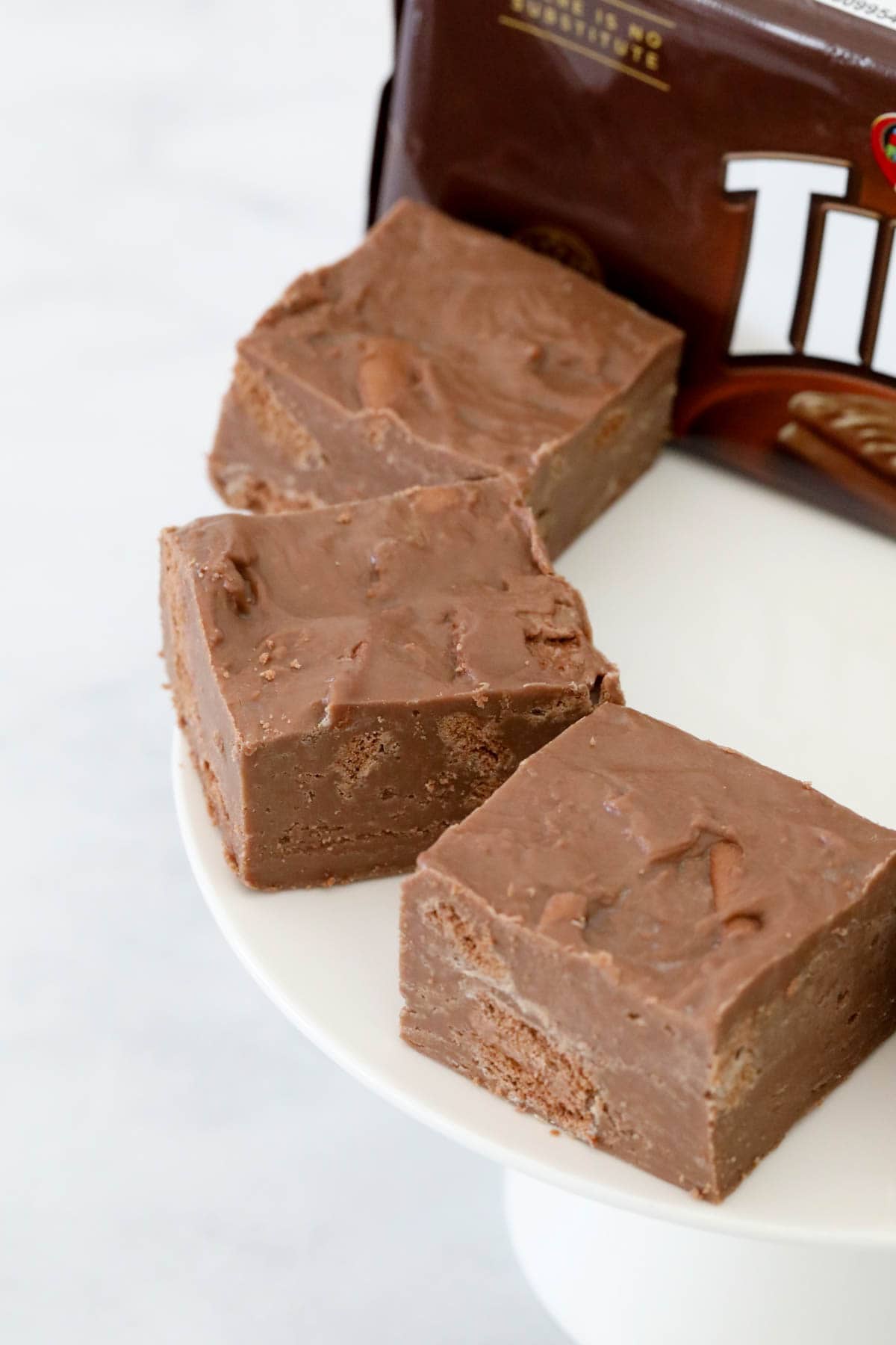 Squares of a chocolate fudge with chunks of Tim Tam, placed around the edge of a cake stand.