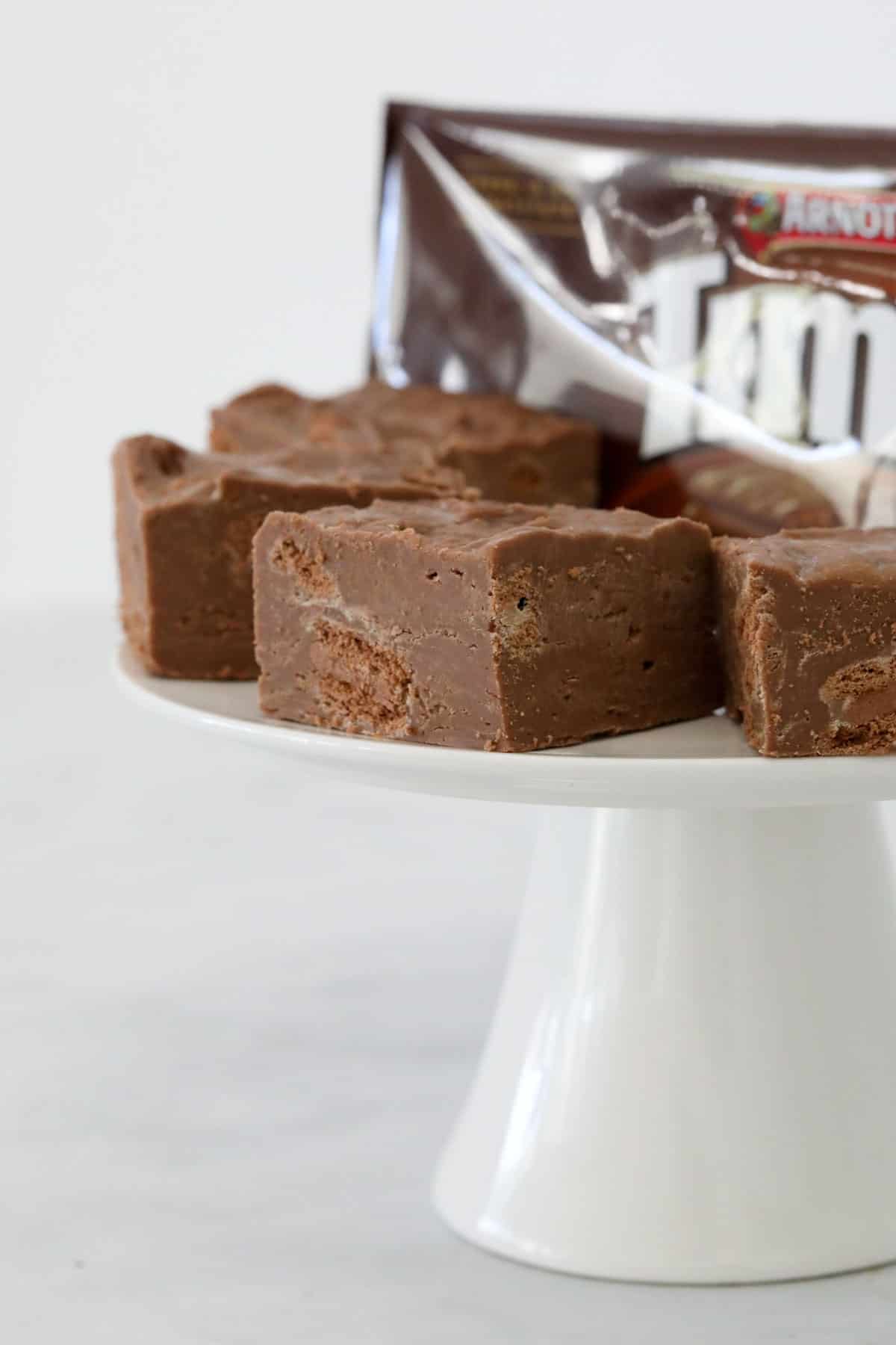 Squares of fudge on a cake stand with a packet of Tim Tam biscuits in the background.