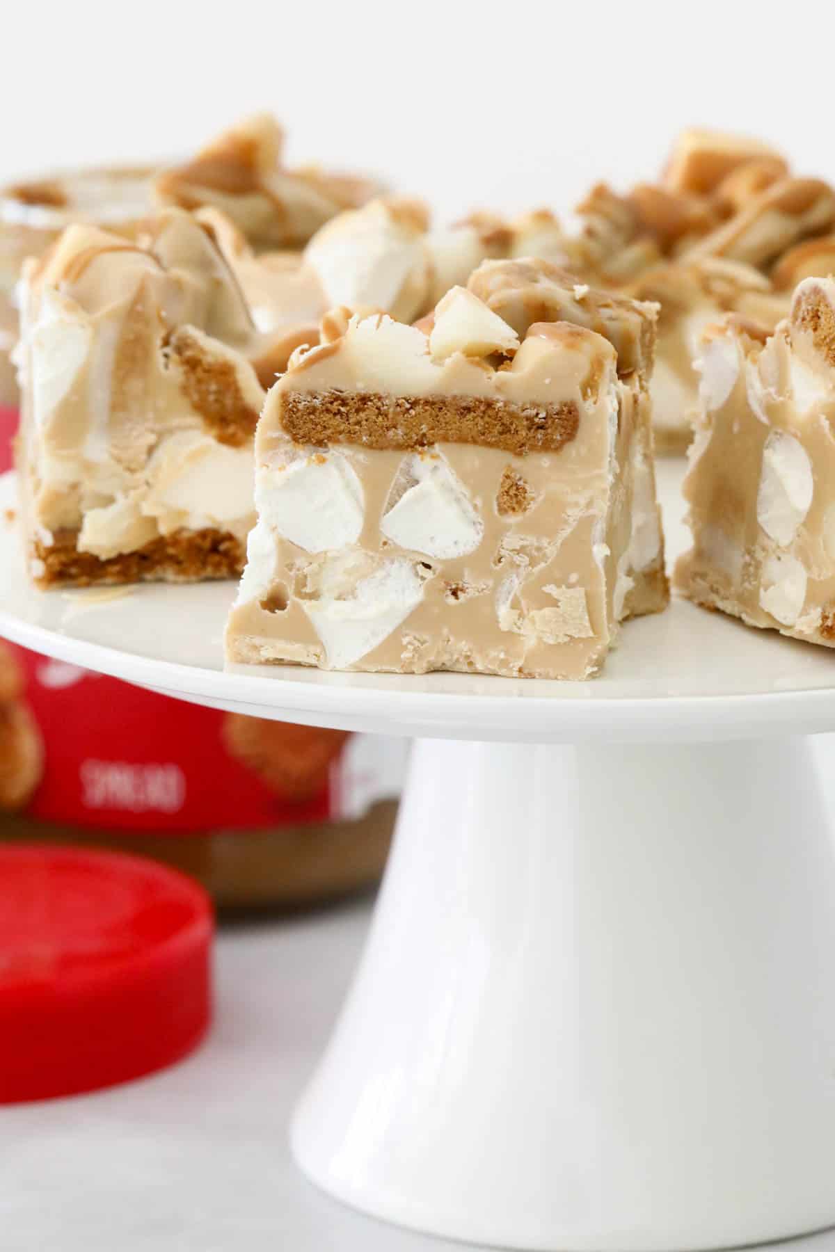 Rocky road on a cake stand, with a jar of Biscoff spread in the background.