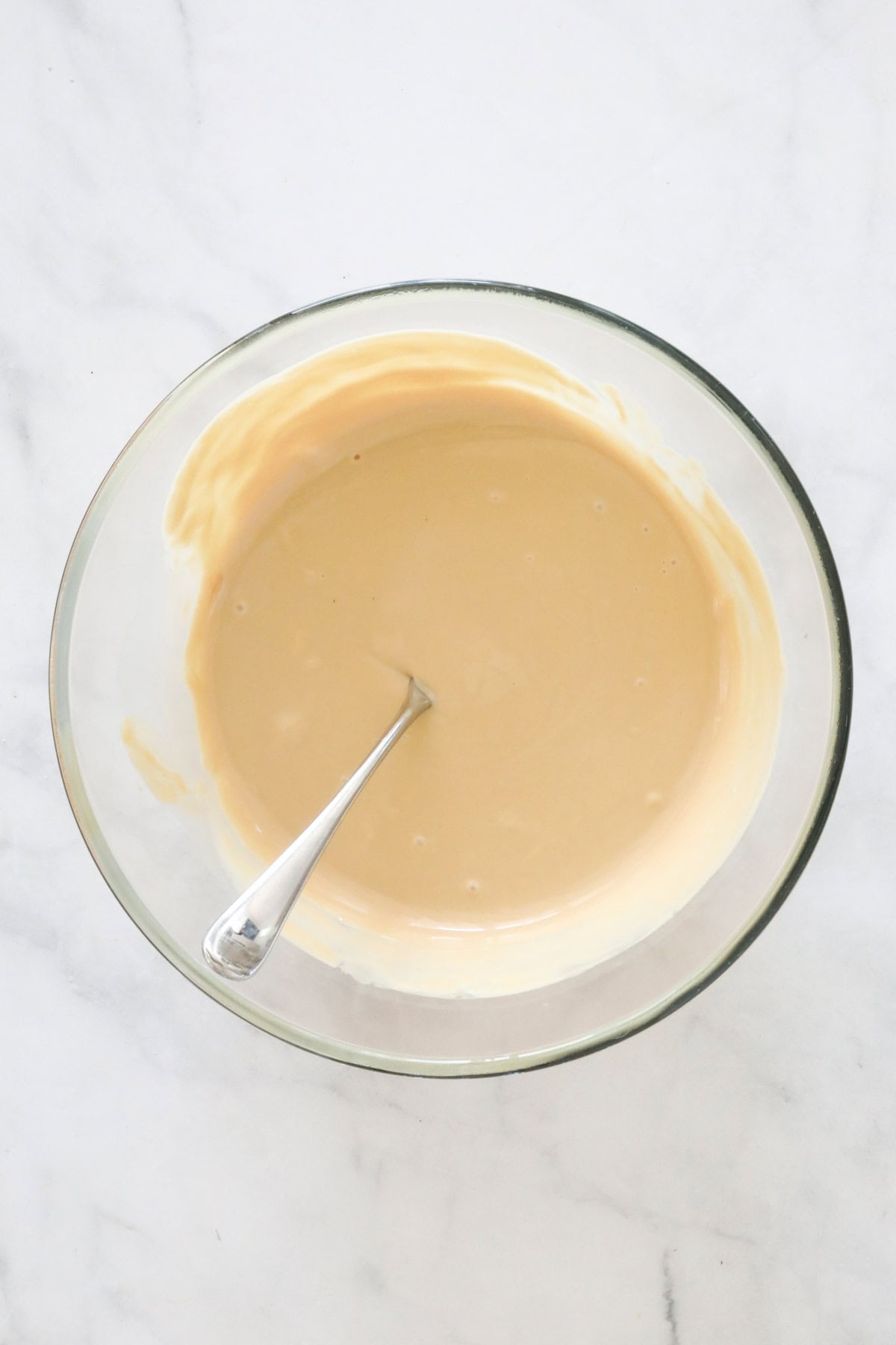 White chocolate and Biscoff spread melted together in a large clear bowl.