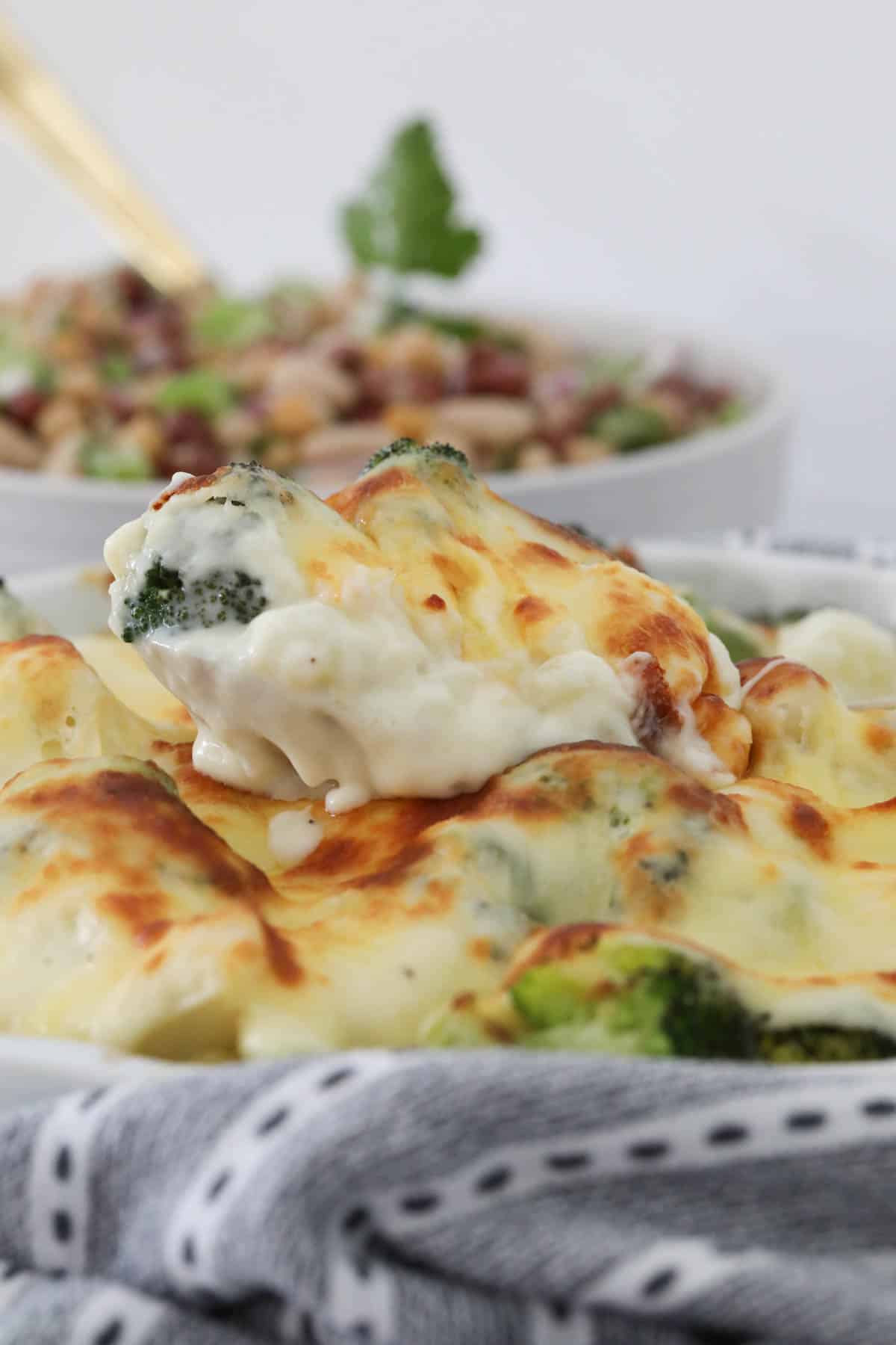 A spoon lifting up a cauliflower and broccoli bake with cheesy mornay sauce.