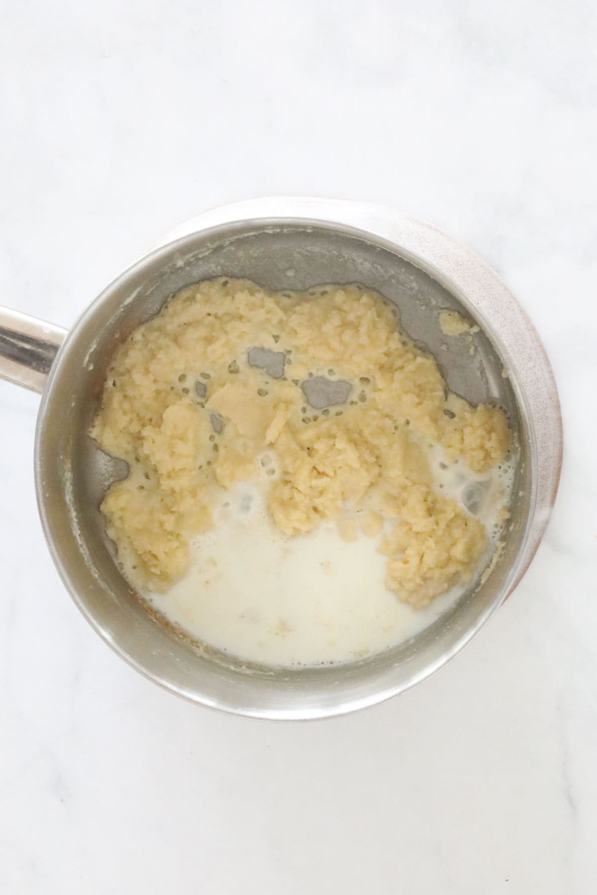 Milk being added to paste in a saucepan.