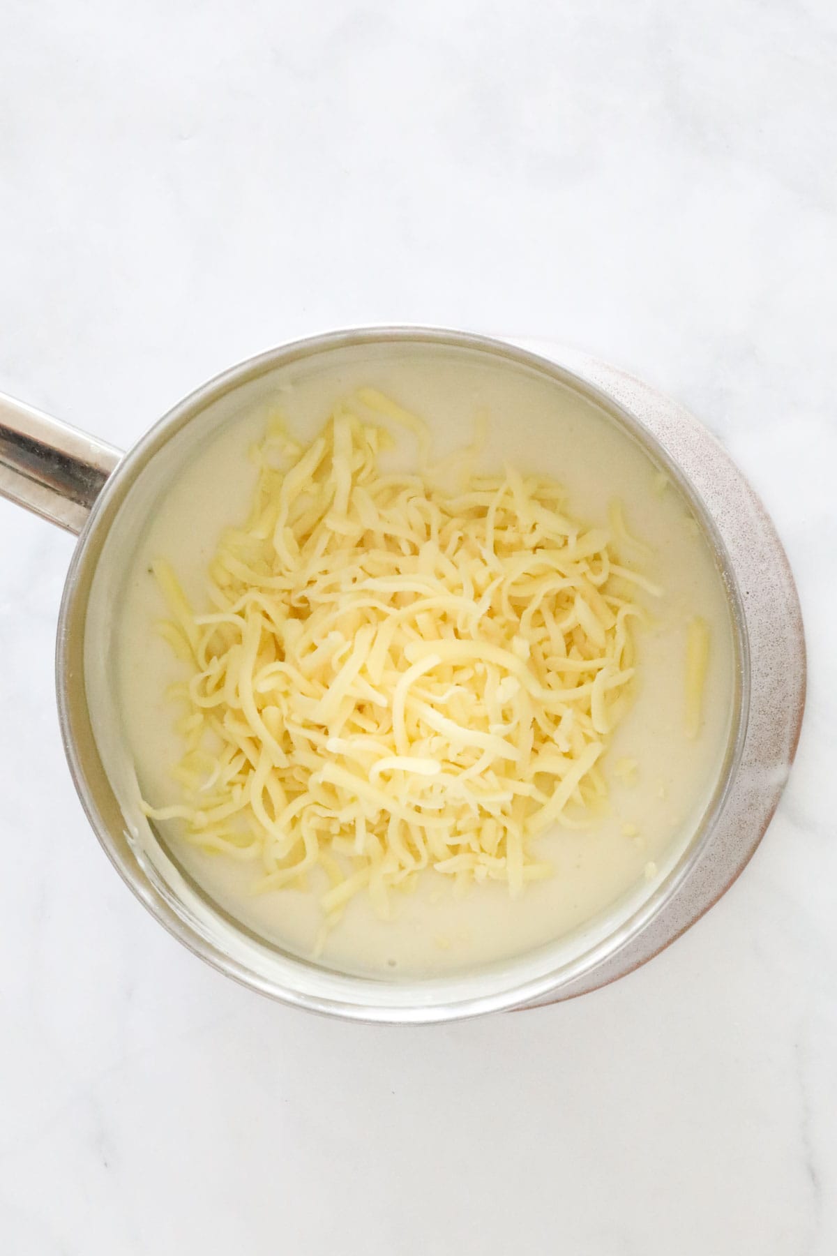 Cheese being added to white sauce in a saucepan.