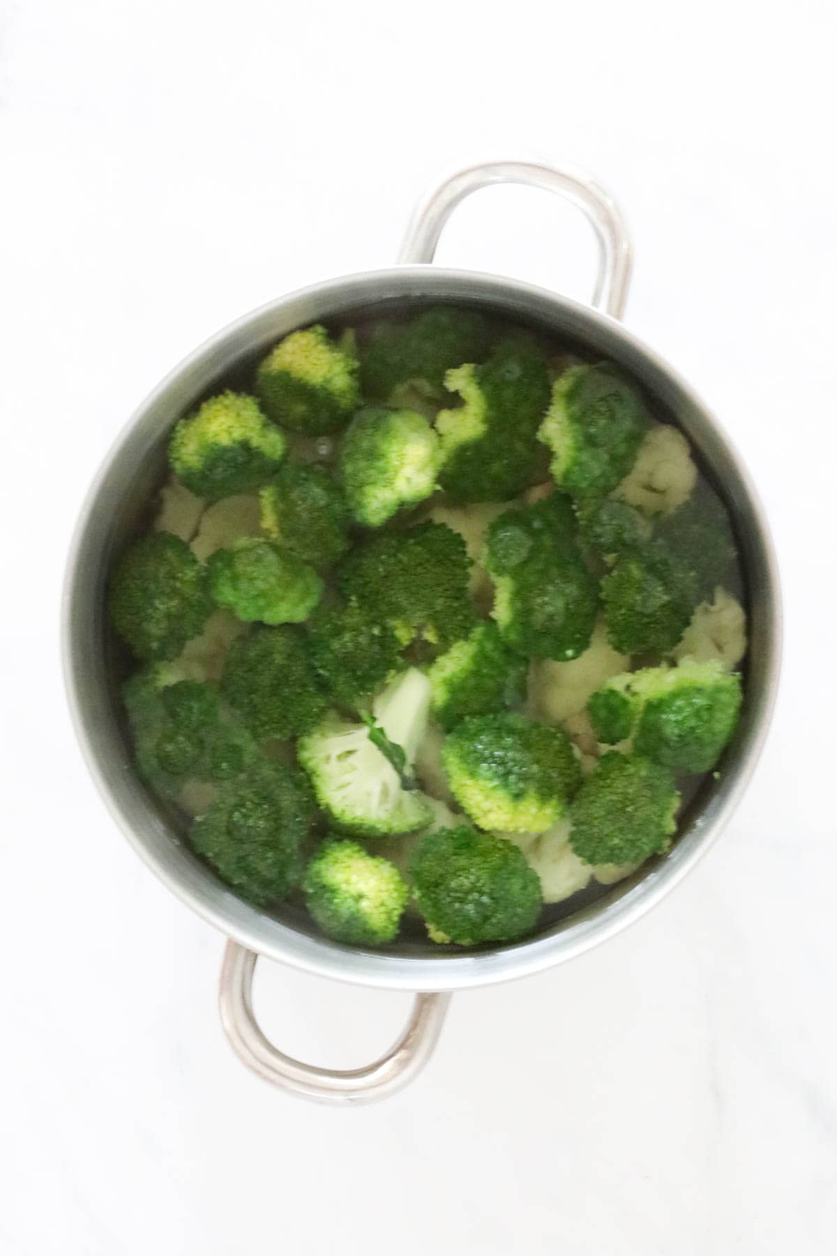 Broccoli cut into florets and placed in a pot.
