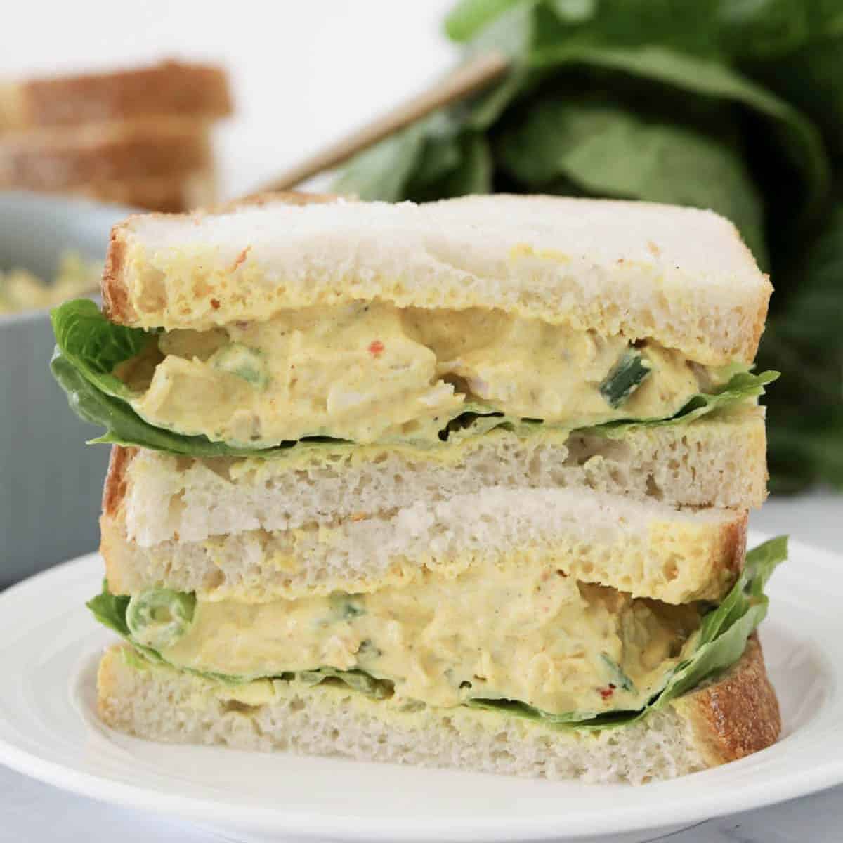A stack of creamy chicken coronation sandwiches with lettuce.
