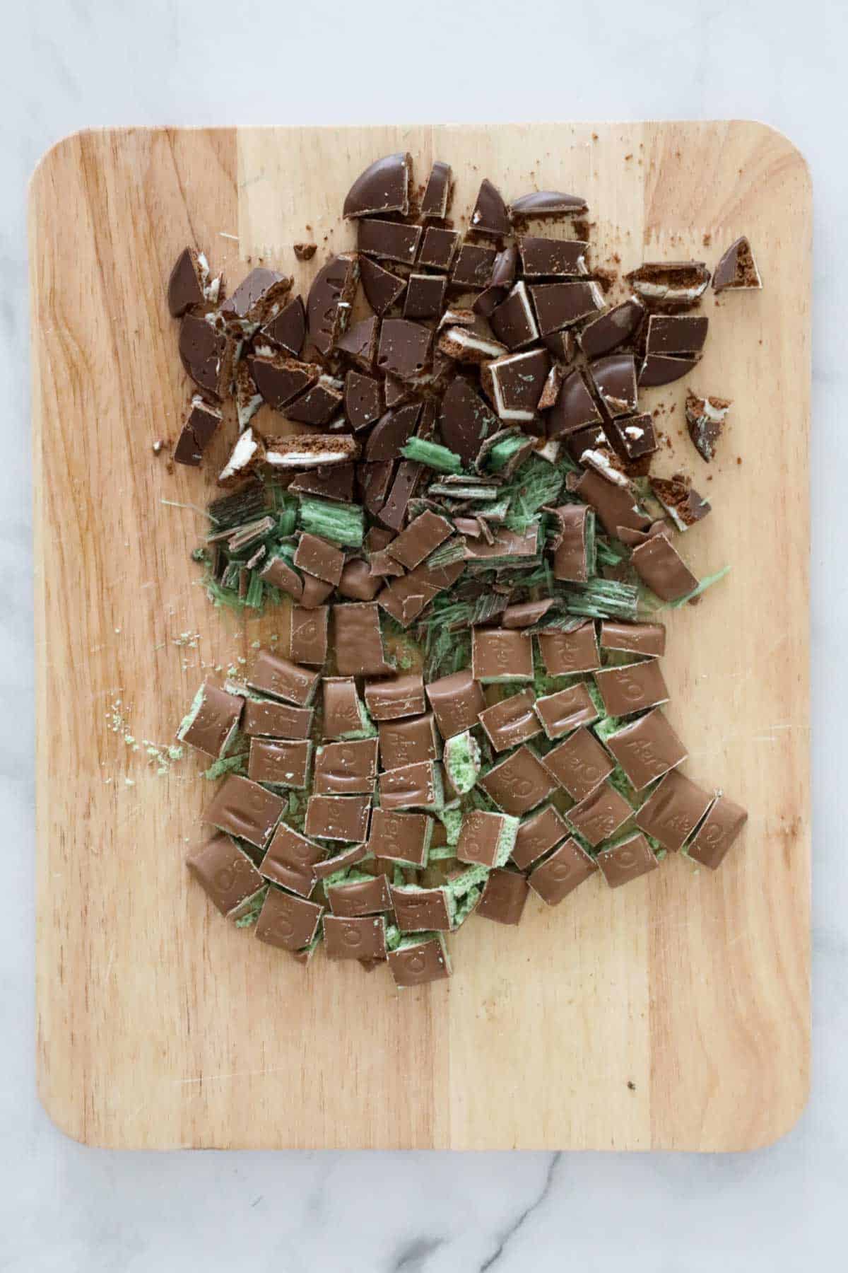 Mint Slice biscuits, Aero Chocolate and Peppermint Crisp bars roughly chopped on a wooden board.