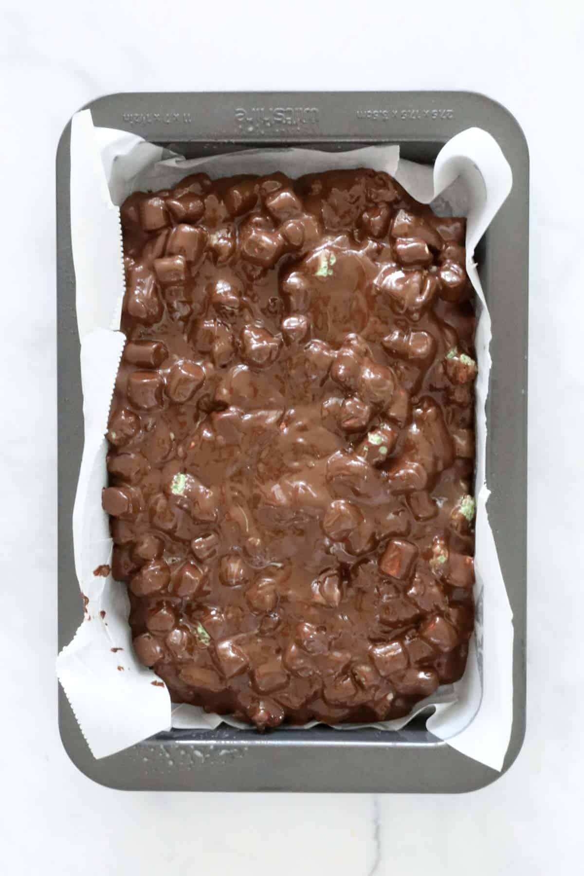 Chocolate, mint and marshmallow mixture spread in a lined baking tray.