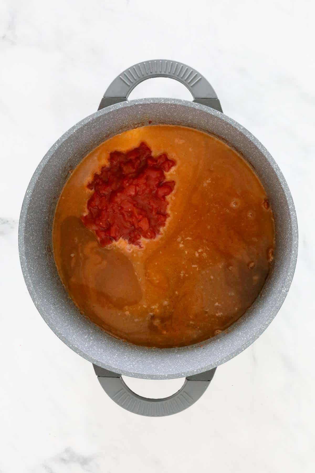 Liquid stock and canned diced tomatoes added to the pan.