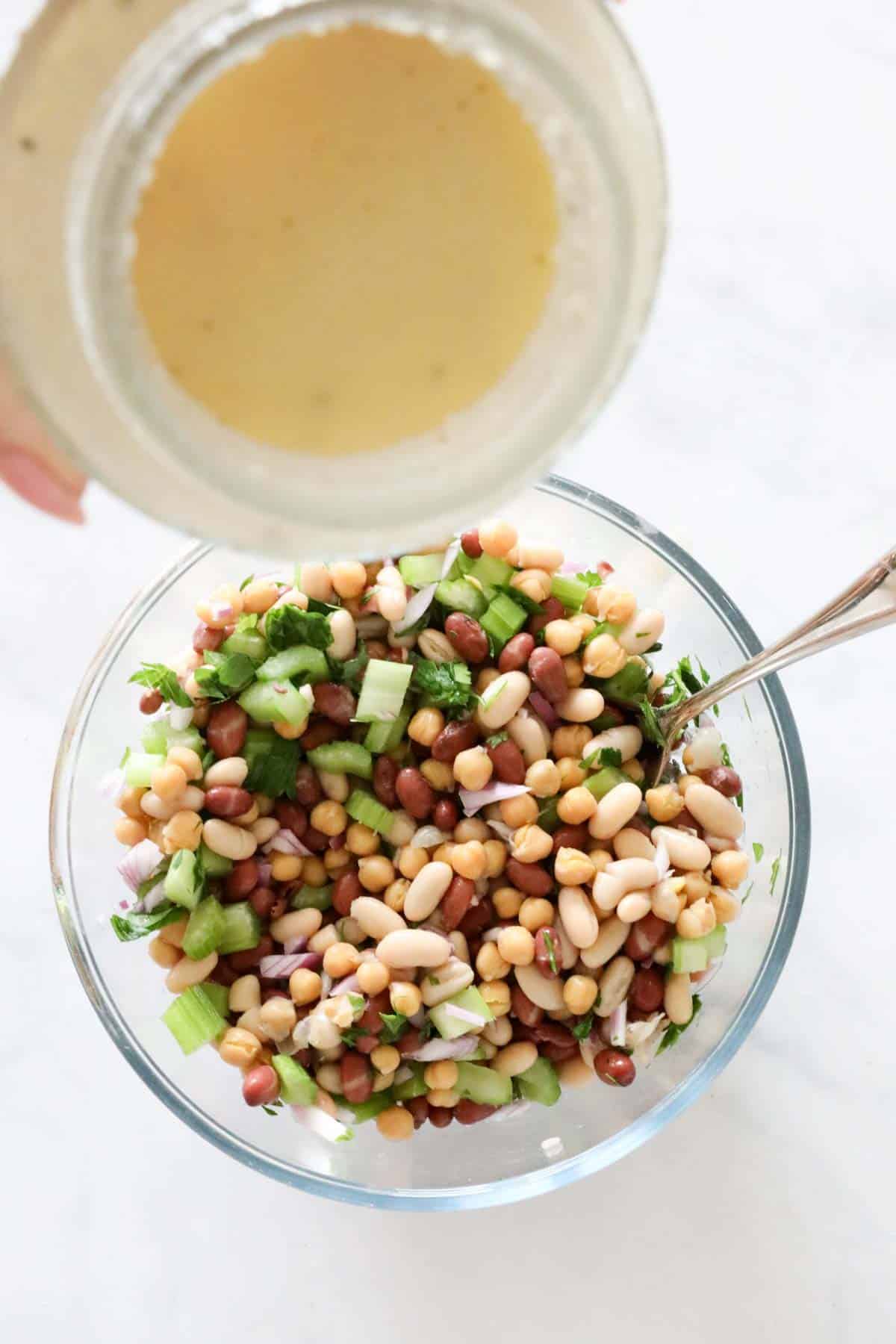 A jar of vinaigrette held above salad ingredients.