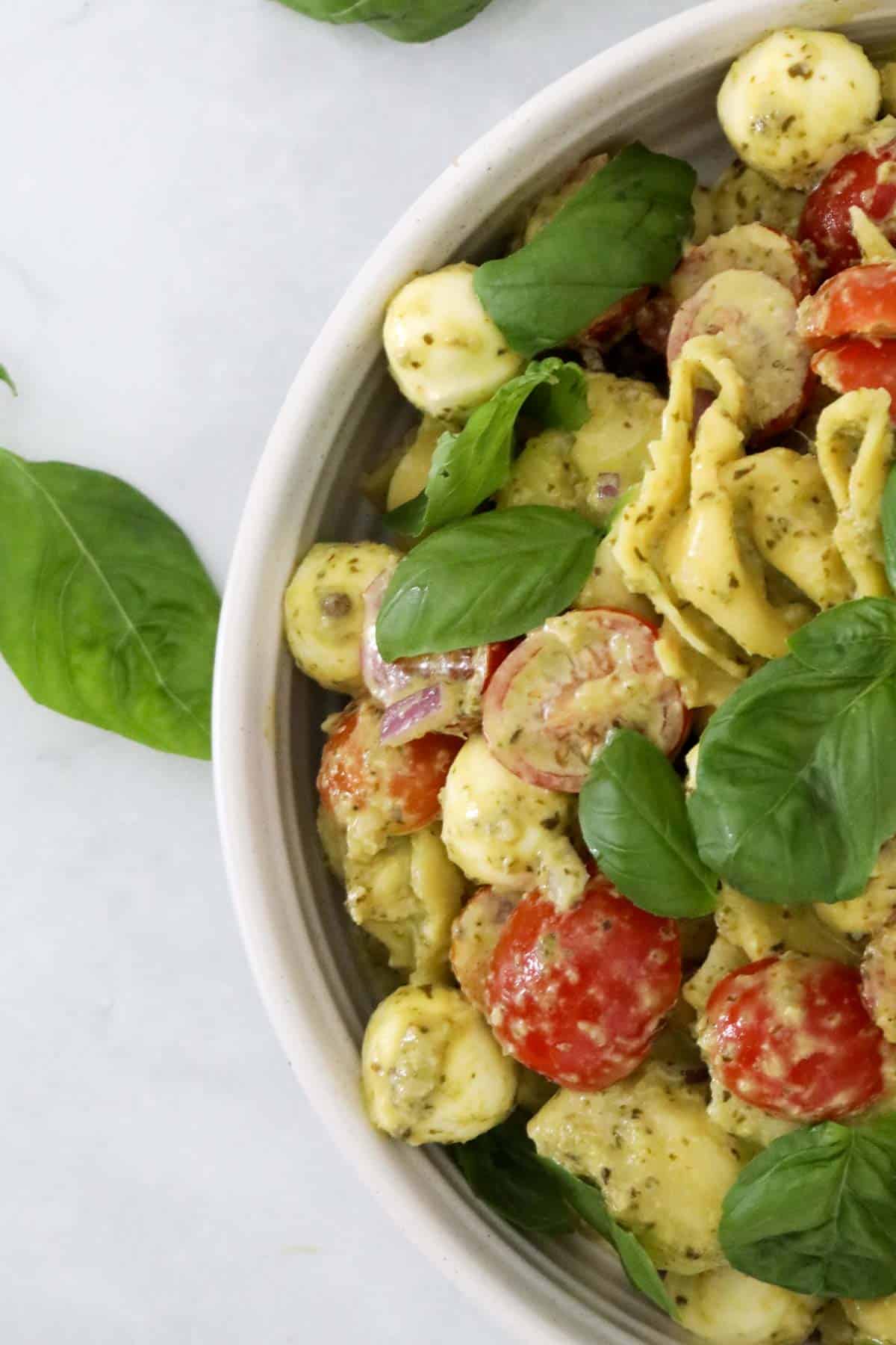 Looking down on a pesto salad with basil leaves on top.