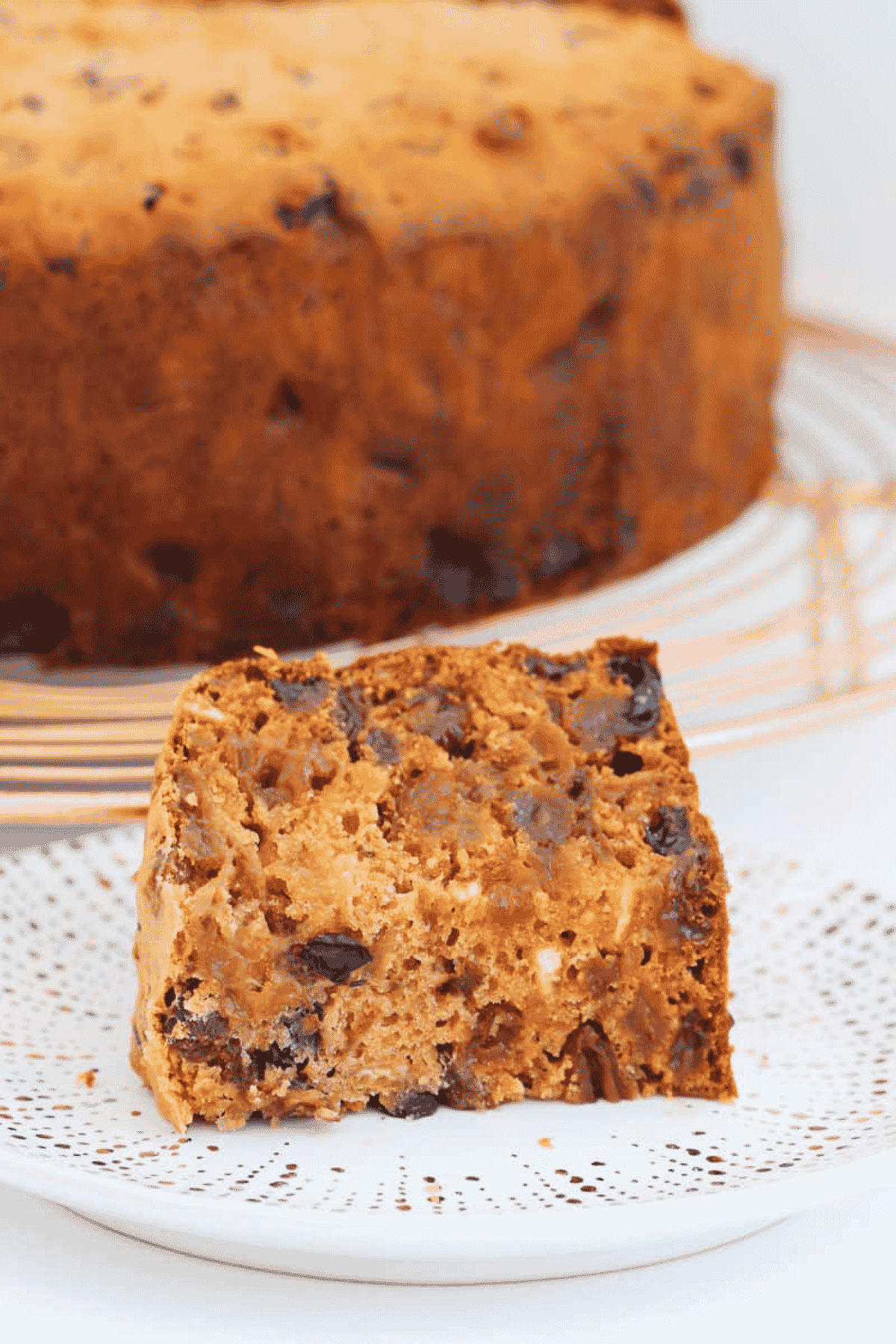 A slice of fruit cake with the entire cake in the background.