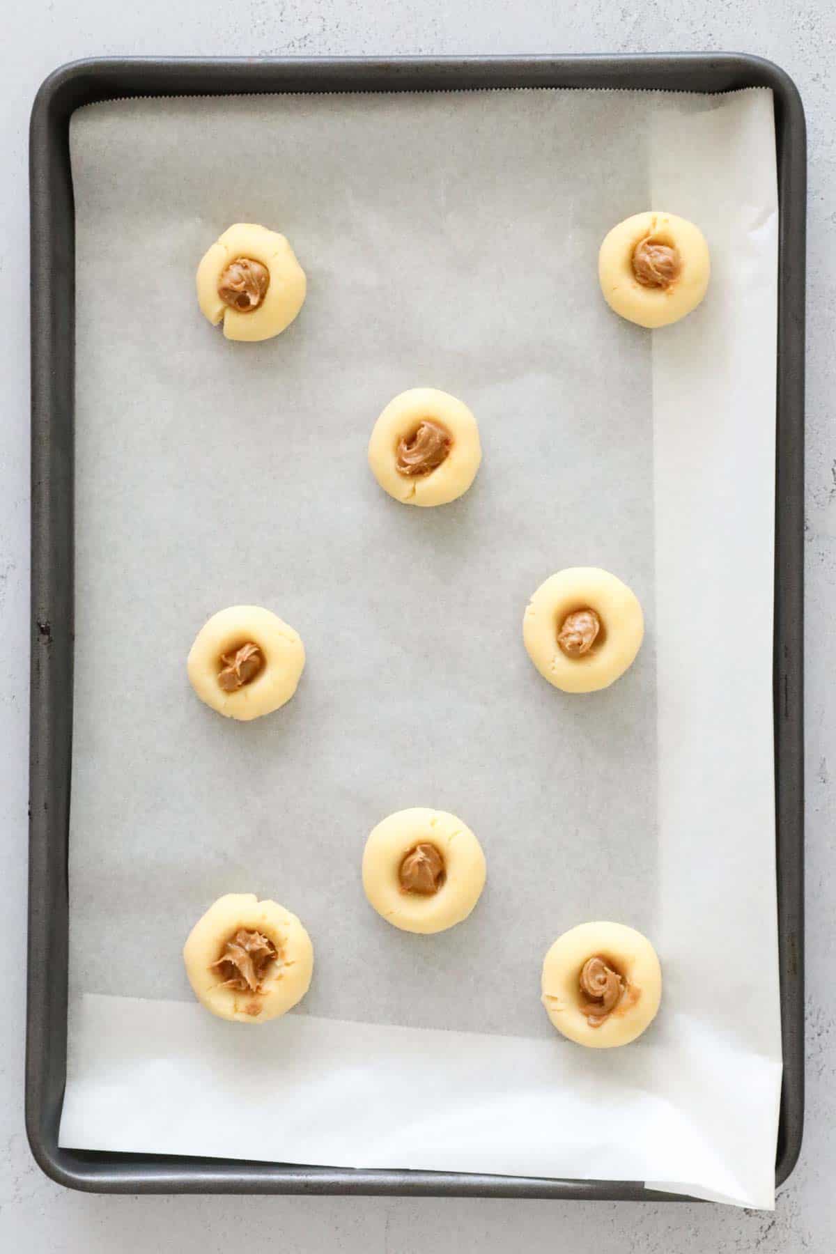 Dough balls on a baking tray with Biscoff spread placed in the indent.