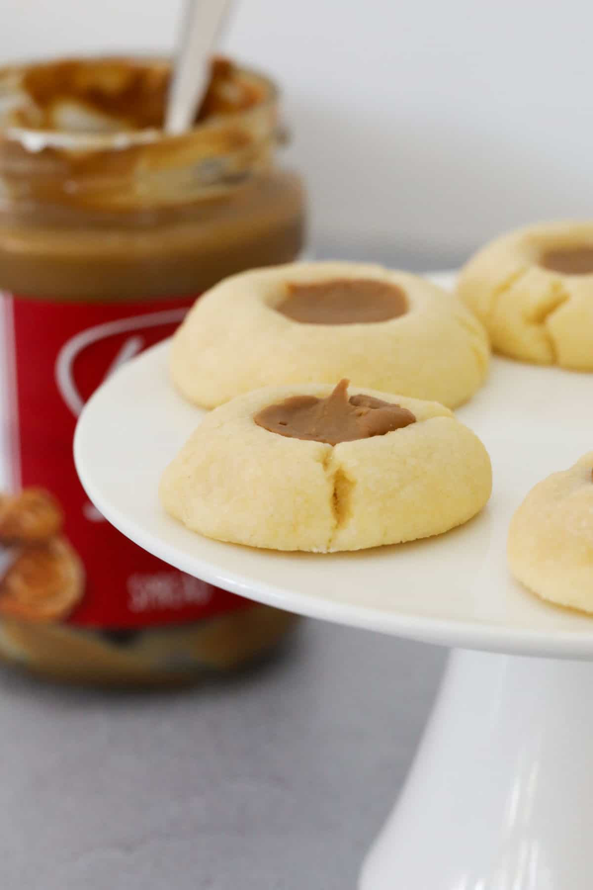 Thumbprint cookies on a white cake tray with a jar of Biscoff in the background.
