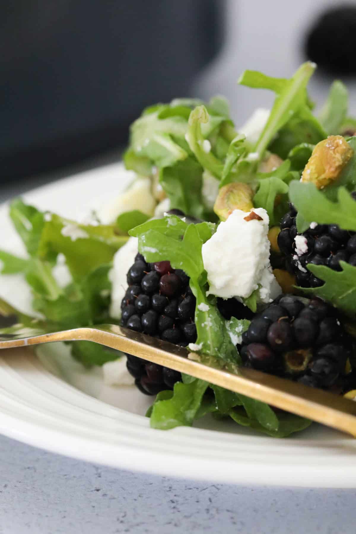 A gold fork on the side of a plate of fresh salad.